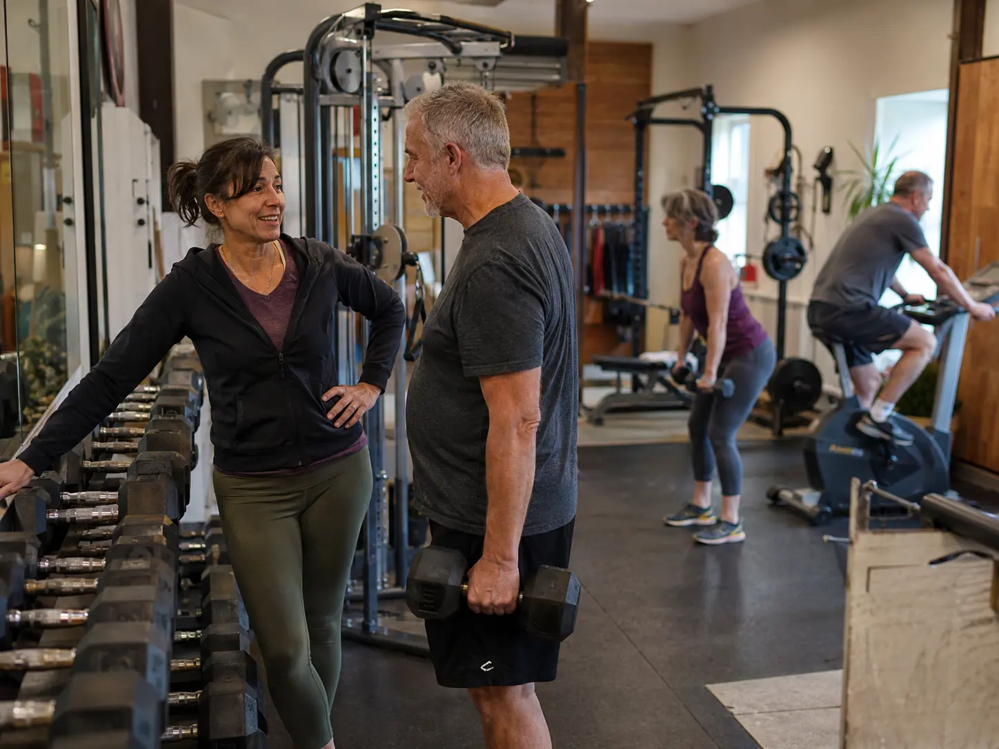 A bright modern fitness studio with a trainer helping a member